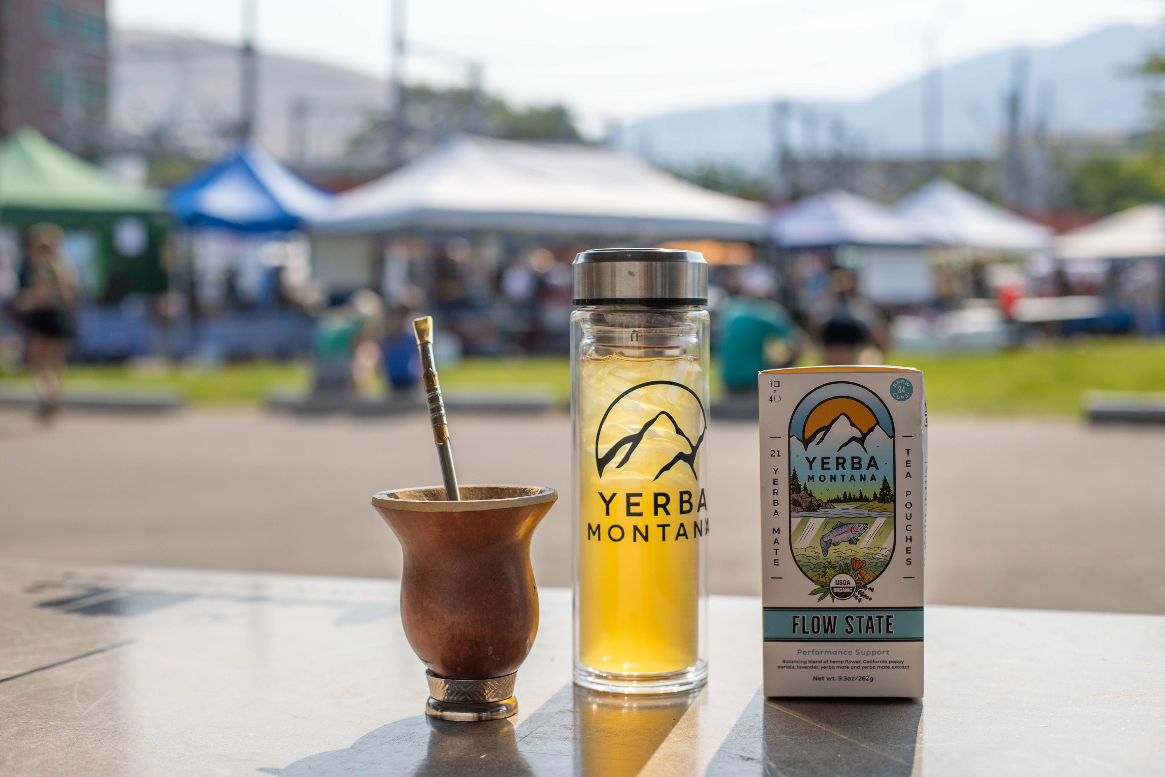 Yerba Montana gourd with bombilla on stone table, glass thermos of iced mate, Flow State tea pouch box.