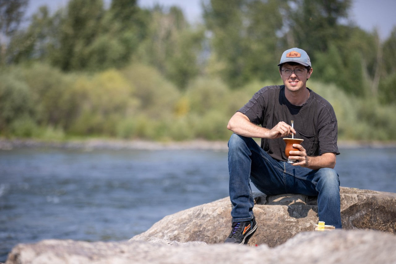 Yerba Montana founder on a rock by a river, holding a mate gourd with bombilla

